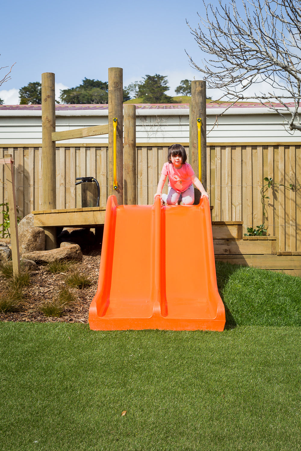A young preschool girl playing on an orange slide at Spotted Frog Preschool