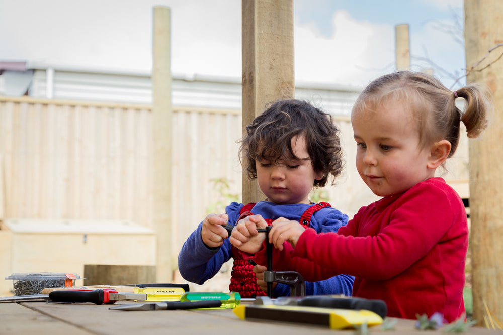 Two girls playing with tools on a workbench at Spotted Frog Preschool