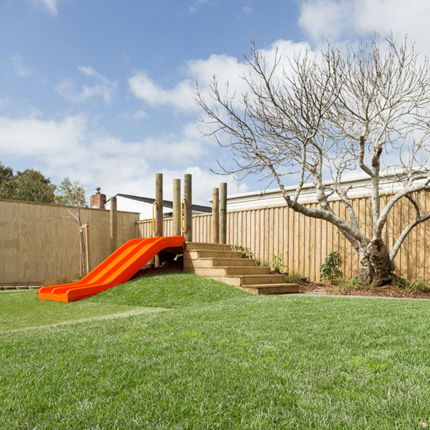 Outdoor shot of an orange slide and green lawn at Spotted Frog Preschool
