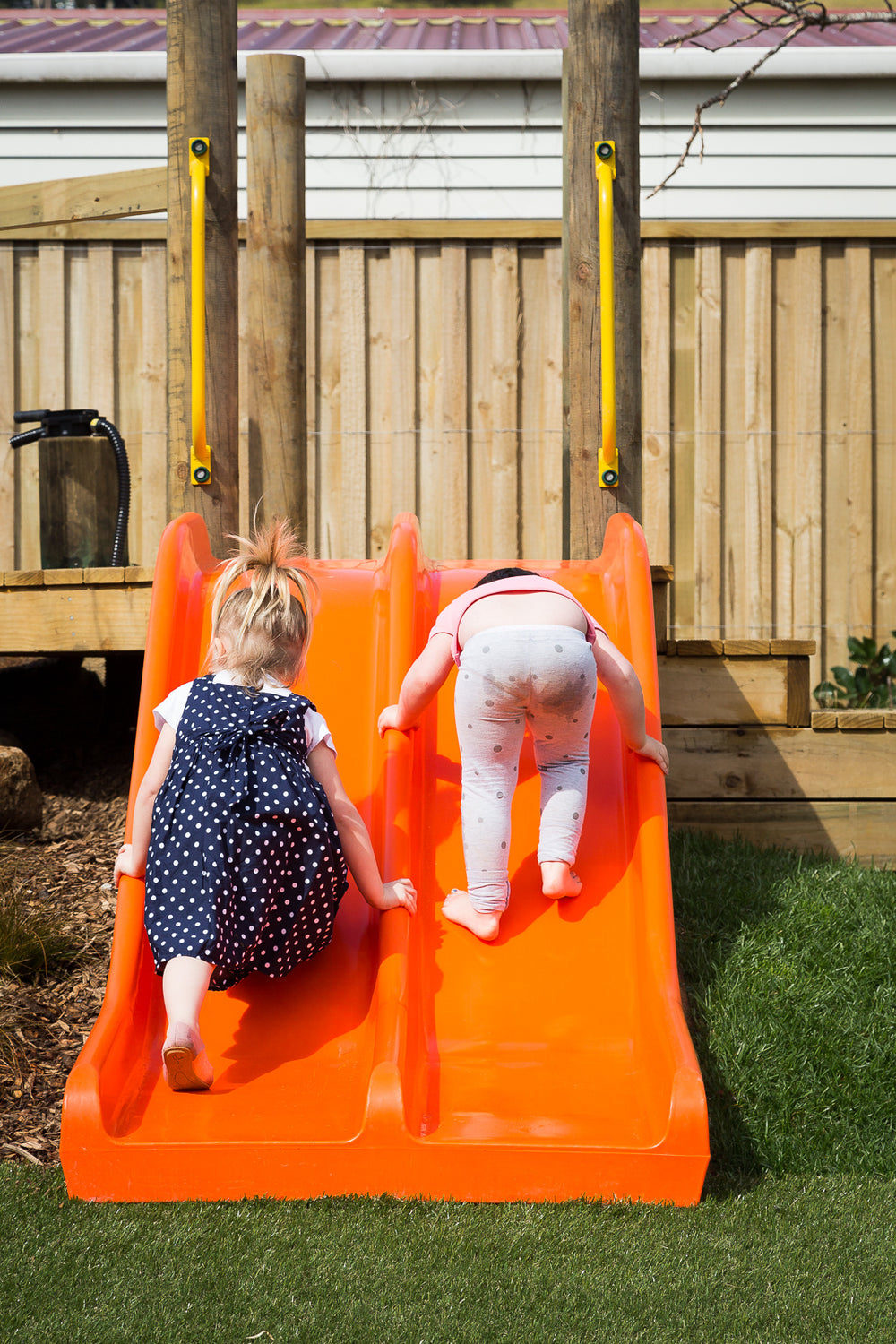 Two girls playing on an orange slide at Spotted Frog Preschool