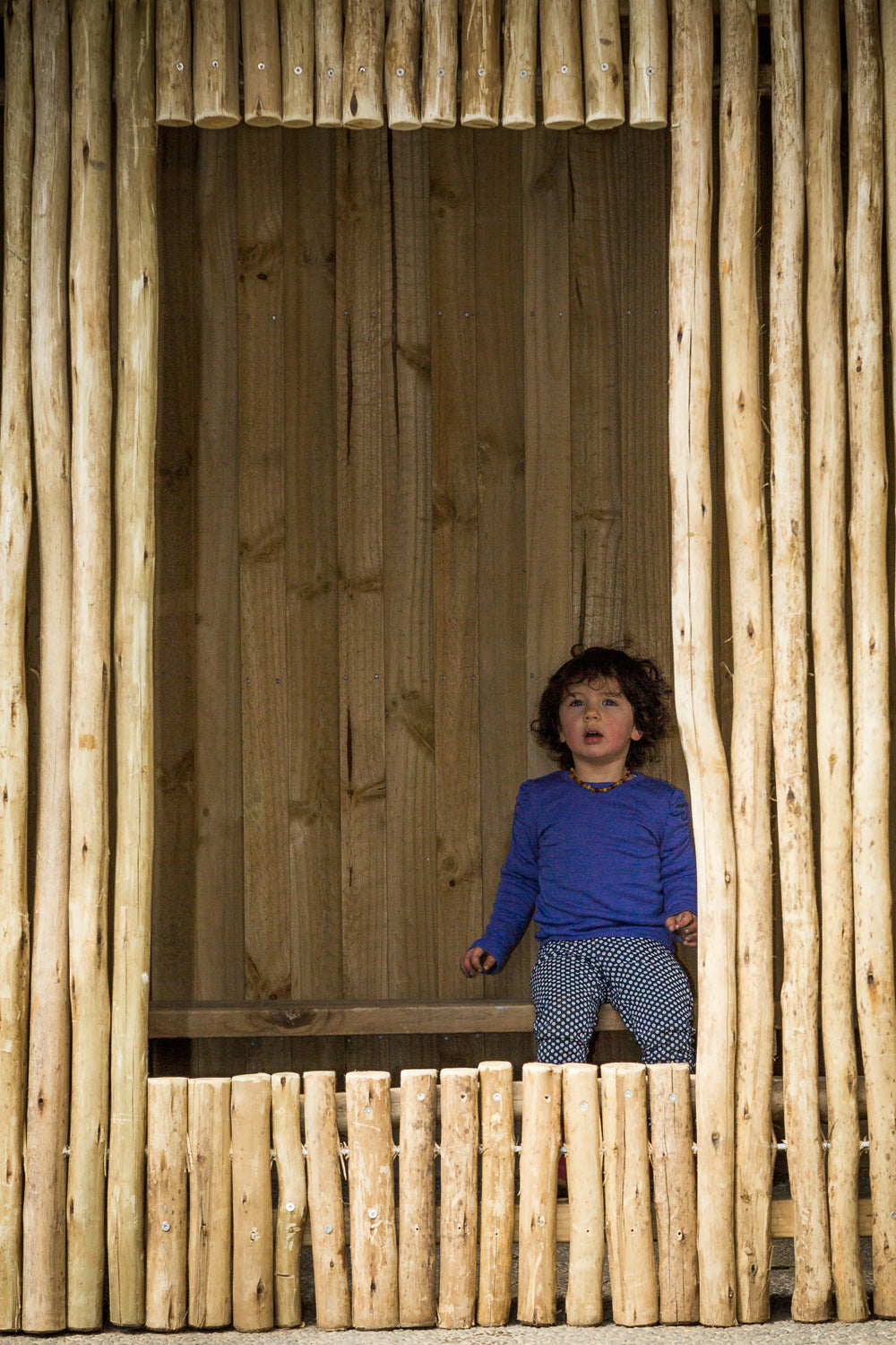 A small girl sitting in a wooden hut at Spotted Frog Preschool