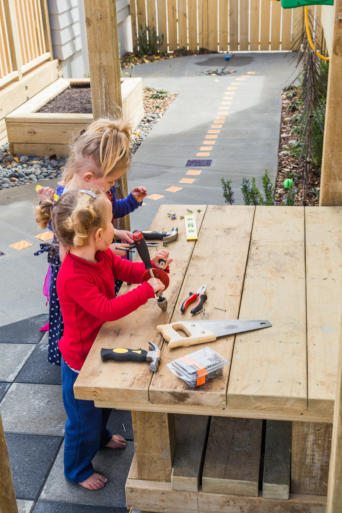 Two preschool girls playing with tools on a workbench at Spotted Frog Preschool