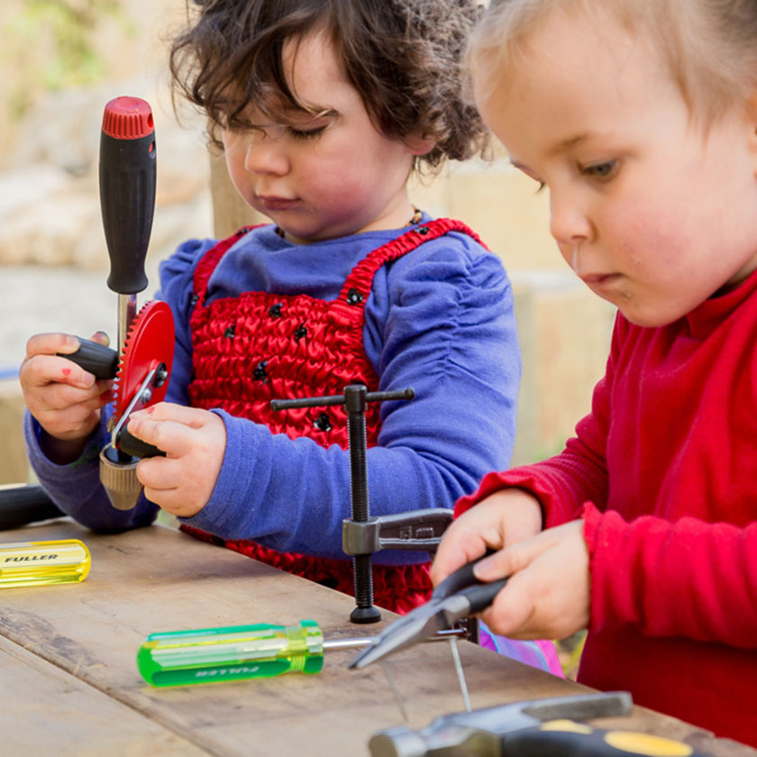 Two preschool girls playing with tools at a workbench at Spotted Frog Preschool