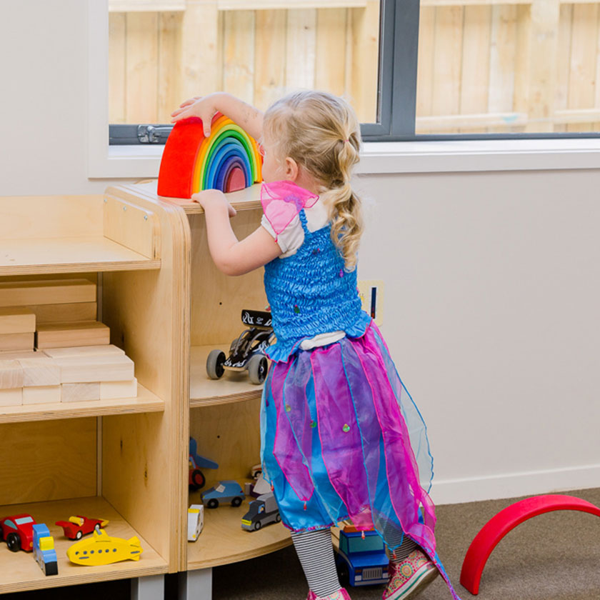 A preschool girl playing with a wooden rainbow at Spotted Frog Preschool